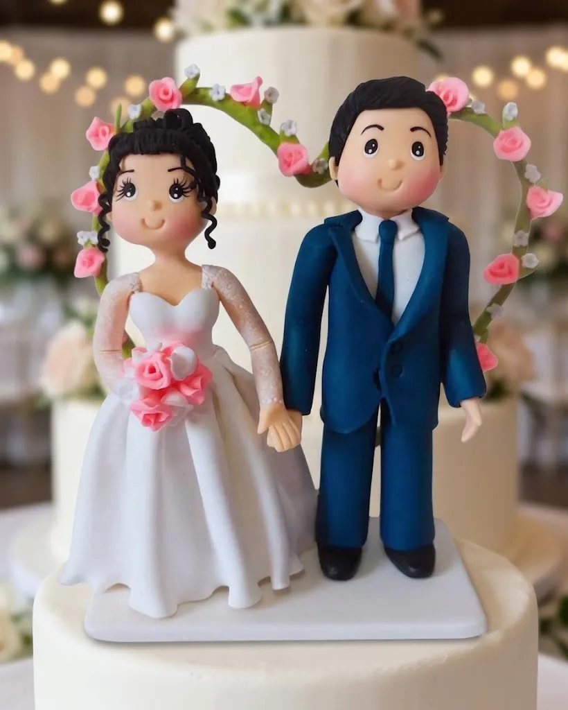 Novios clásicos hechos a mano bajo un arco de rosas, sobre una torta de matrimonio blanca