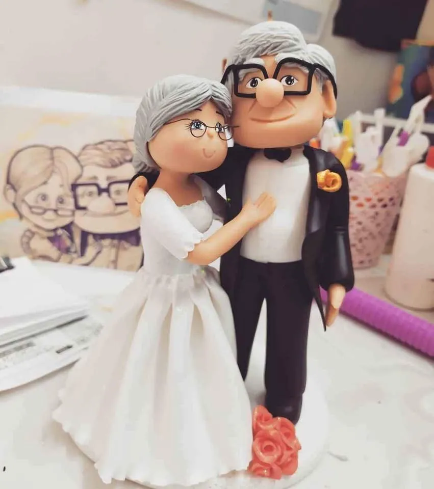 Pareja de novios mayores modelada a mano, sobre la mesa del taller junto al boceto que le dio origen